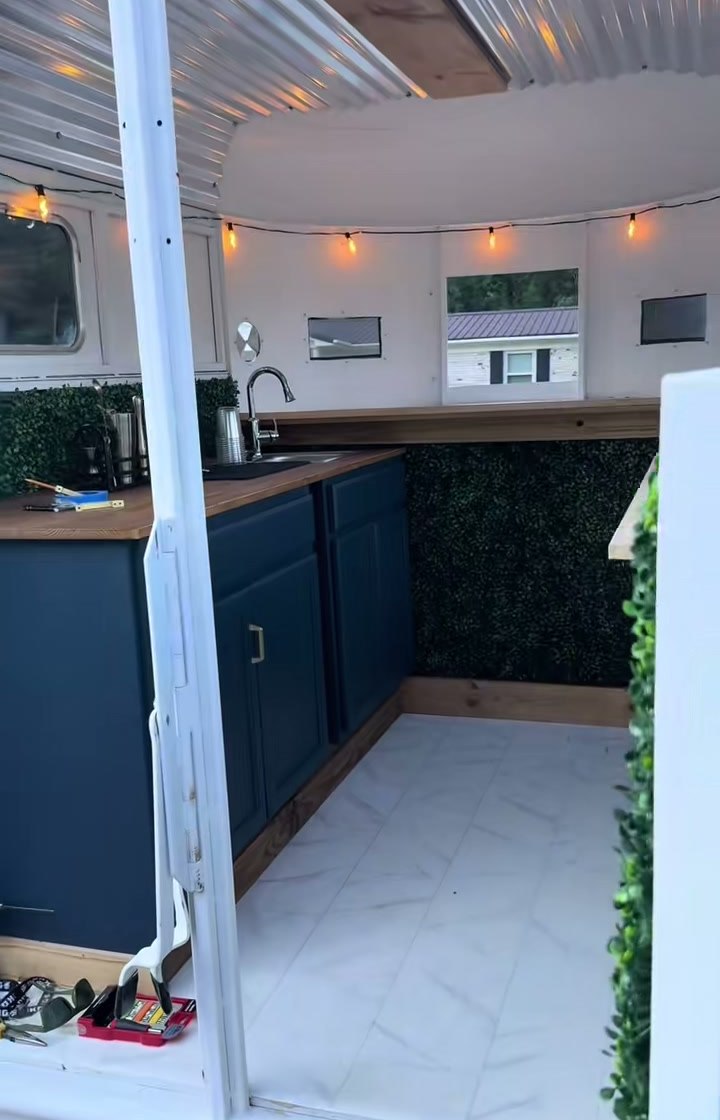 Inside the trailer: navy cabinets, a butcher block counter, a sink, boxwood hedge walls and warm string lights