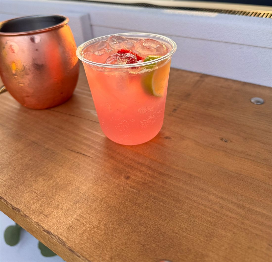 A strawberry drink over ice with fresh lime, beside a copper mug on the bar