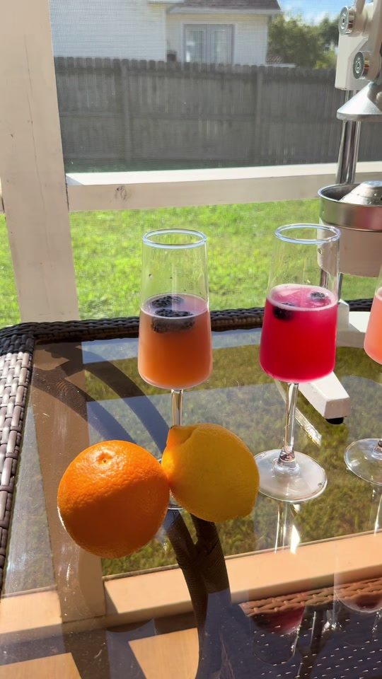 Two mimosas with blackberries beside a whole orange and lemon